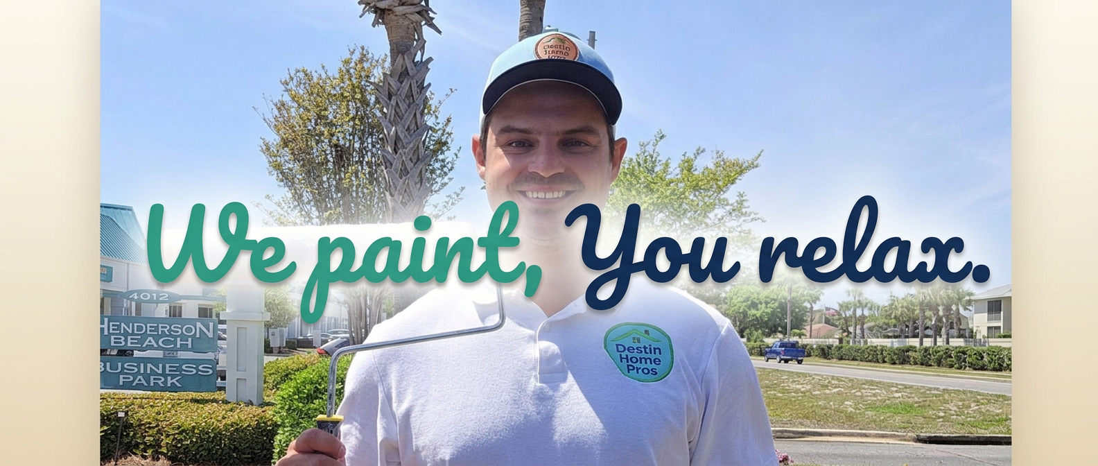 Nick Zellmer, owner of Destin Home Pros, holding a paint roller in front of the Henderson Beach Business Park sign with We Paint, You Relax on the sign
